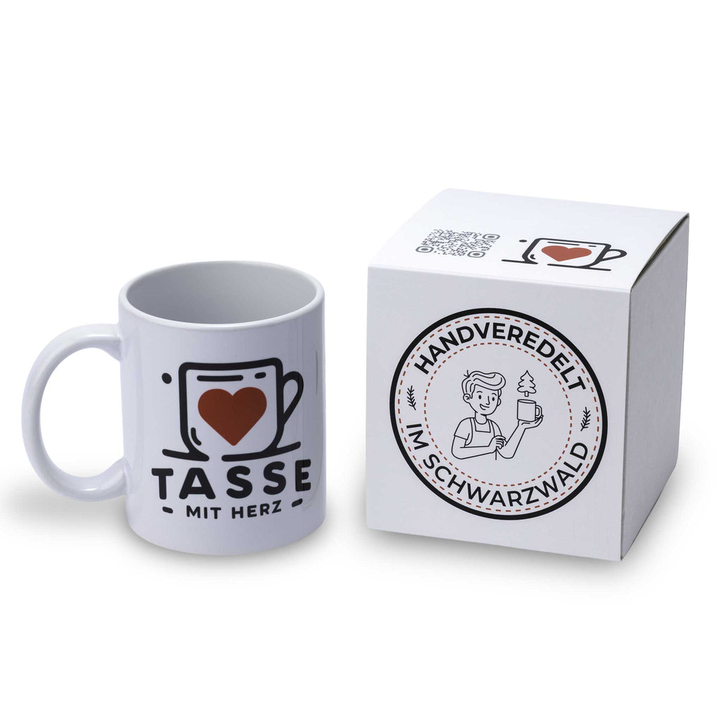 Personalisierte weiße Fototasse von Tasse mit Herz neben einem edlen weißen Geschenkkarton mit dem runden Siegel „Handveredelt im Schwarzwald“.